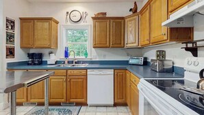 A kitchen with wooden cabinets, a dishwasher, a stove, and a window with a view of greenery. - Tranquil Dog- Friendly Riverfront Home with Fill Kitchen and WIFI (Arden)