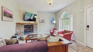 A living room with a fireplace, a television, a pink sofa, and a door with a window. - Tranquil Dog- Friendly Riverfront Home with Fill Kitchen and WIFI (Arden)