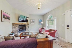 Ein Wohnzimmer mit Kamin, Fernseher, einem rosafarbenen Sofa und einer Tür mit Fenster.