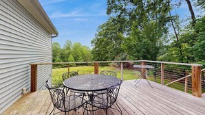 A deck with a metal table and chairs, a small grill, and a view of a green landscape. - Tranquil Dog- Friendly Riverfront Home with Fill Kitchen and WIFI (Arden)