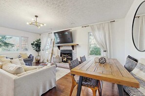 A spacious living room with a fireplace, a dining table, and a sofa. - Charming 4BR retreat with Full Kitchen, Wifi and Patio | Pet-friendly (Arden)
