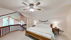 Un dormitorio con cama de madera, ventilador de techo, mesita de noche, lámpara y vista a un balcón.