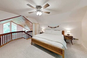 Ein Schlafzimmer mit einem hölzernen Bett, einem Deckenventilator, einem Nachttisch, einer Lampe und Blick auf einen Balkon.