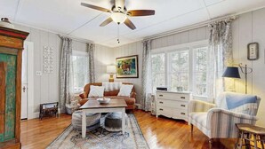A room with a ceiling fan, a sofa, a coffee table, a patterned rug, a window with curtains, and a lamp. - Bearcat Cottage (Lake Junaluska)