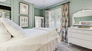 A bedroom with a bed, dresser, and framed botanical prints on the wall. - Bearcat Cottage (Lake Junaluska)