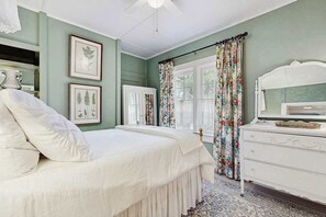 Ein Schlafzimmer mit Bett, Schminktisch und gerahmten Pflanzenbildern an der Wand.