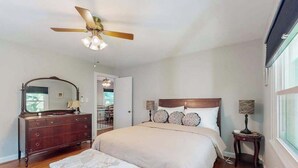 Ein Schlafzimmer mit Bett, Schminktisch, Spiegel, Deckenventilator und Fenster.