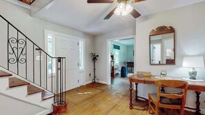 Eine Treppe mit Holzgeländer, ein Deckenventilator, ein Holzesstisch mit Stühlen und ein Spiegel an der Wand.
