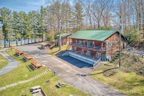 A wooden cabin with a green roof, a covered porch, and a parking area.