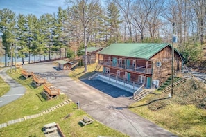 A cabin with a green roof, a porch, and a parking area.