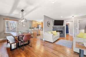 Ein modernes Wohnzimmer mit Kamin, ein Essbereich mit Holztisch und Stühlen sowie eine Küche im Hintergrund.