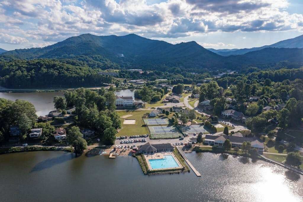 An aerial view of a lakeside property with a swimming pool, houses, and a large building.