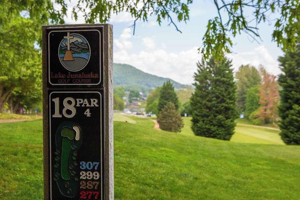 A golf course sign with a cross and a mountain landscape in the background.