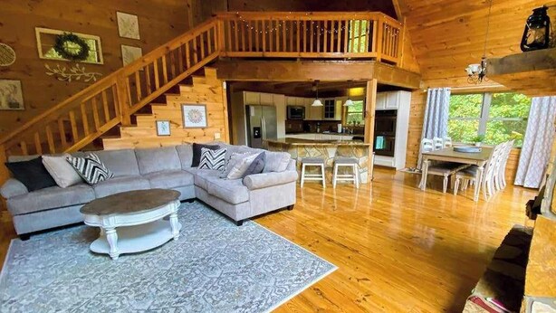Een houten cabin met een woonkamer, eethoek, keuken en een trap naar een verdieping.
