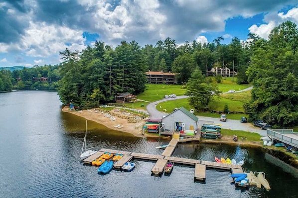 A lakeside lodge with a dock, boats, and a building surrounded by trees.