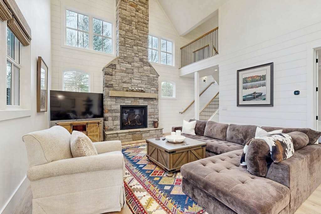 A spacious living room with a stone fireplace, a large sofa, a television, and a staircase.