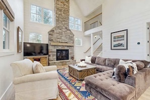 A spacious living room with a stone fireplace, a large sofa, a television, and a staircase.