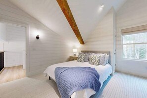 Ein Schlafzimmer mit einem großen Bett, einem Holzbalken an der Decke, einem Nachttisch mit Lampe und einem Fenster mit Blick.