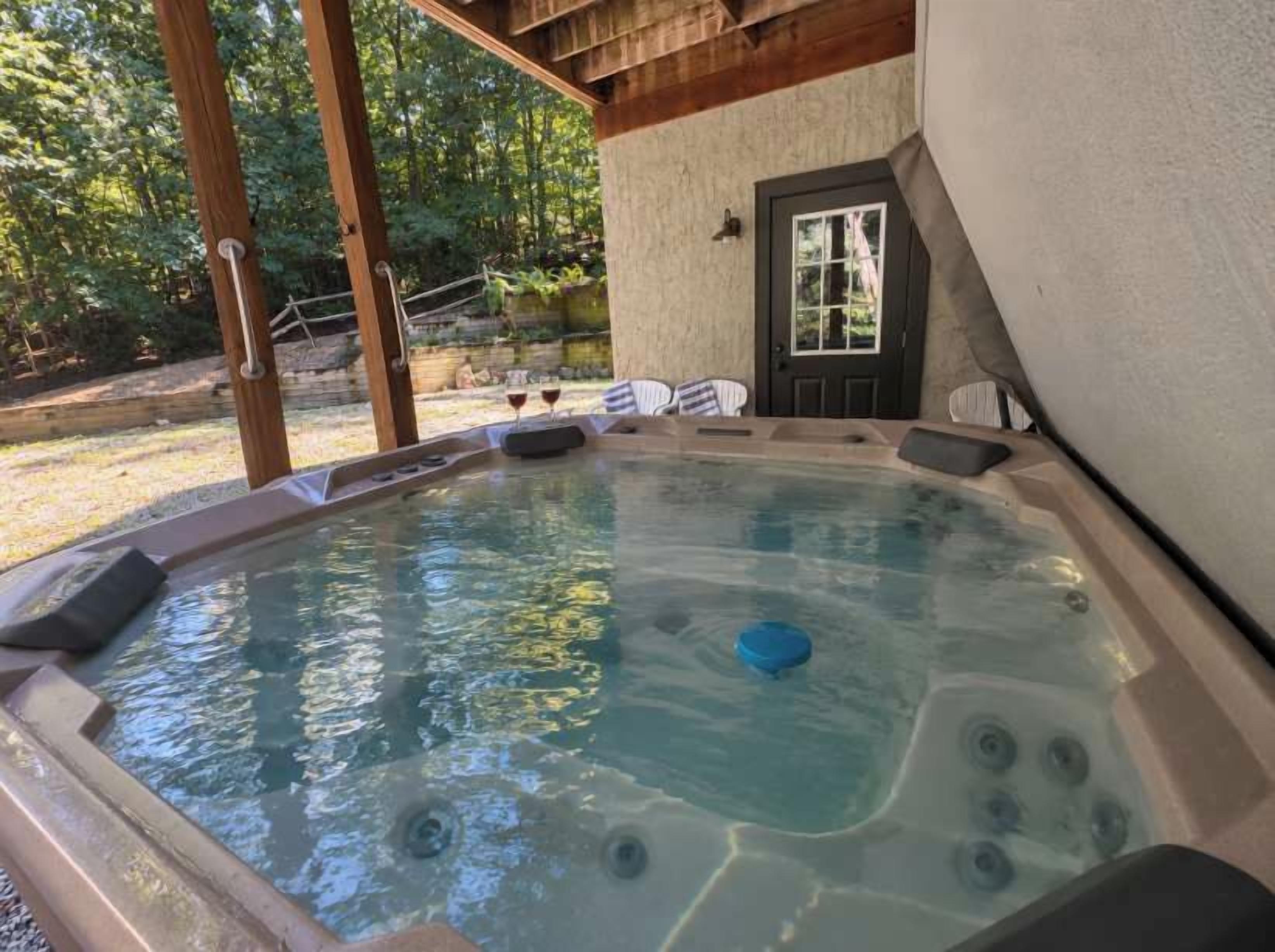 A hot tub with a wooden deck, a door, and a view of trees.