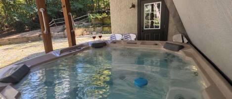 A hot tub with a wooden deck, a door, and a view of trees.