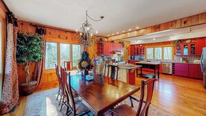 Un interior de madera con una mesa de comedor, sillas, una araña y una zona de cocina.