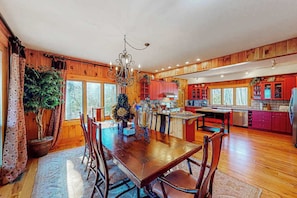 A wooden interior with a dining table, chairs, a chandelier, and a kitchen area. - Updated mountain view cabin with vaulted ceilings, large deck, & chef's kitchen (Sapphire)