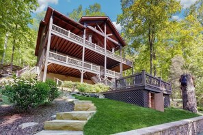 Eine zweistöckige Holzhütte mit Balkon, umgeben von einem gepflegten Rasen und Bäumen.
