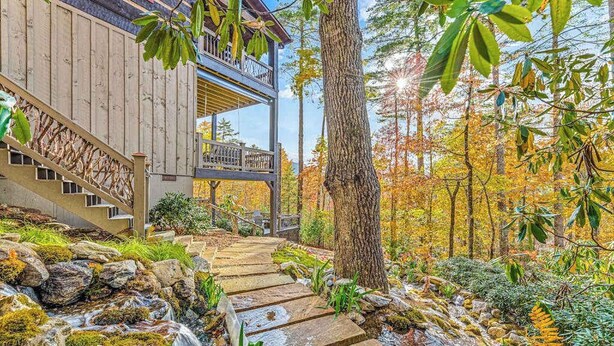 Un bâtiment en bois avec un escalier en pierre menant à un balcon, entouré d’un feuillage automnal et traversé par un petit ruisseau.