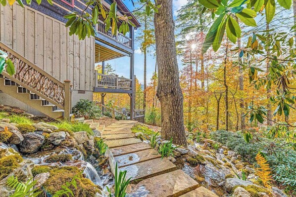 Ein Holzgebäude mit einer Steinstufe, die zu einem Balkon führt, umgeben von Herbstlaub und einem kleinen Bach.