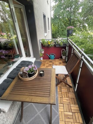 Een balkon met een houten tafel, stoelen en bloempotten.