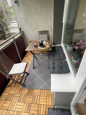 Een balkon met een houten tafel, een comfortabele bank, een stoel en een bloempot.