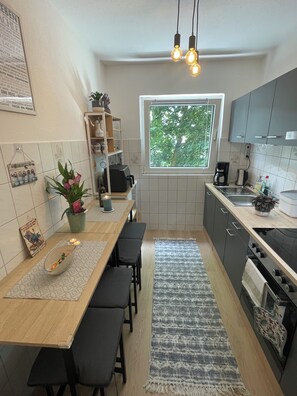 Een moderne keuken met een eethoek, een raam met uitzicht op bomen, en een klein plantje op het aanrecht.
