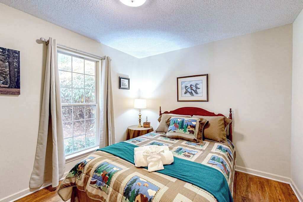 Een slaapkamer met een bed, een raam met gordijnen, een bedlampje en ingelijste foto's aan de muur.
