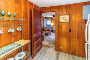 A wooden interior with a door leading to another room, shelves with glassware, and a dining table. - Charlotte Cabin (Waynesville)