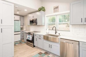 A modern kitchen with white cabinets, stainless steel appliances, a window with blinds, and a tiled backsplash. - Contemporary dog-friendly mountain home with firepit, grill, enclosed backyard (Swannanoa)
