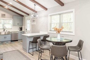 A modern kitchen with a central island, bar stools, and a dining table with chairs. - Contemporary dog-friendly mountain home with firepit, grill, enclosed backyard (Swannanoa)