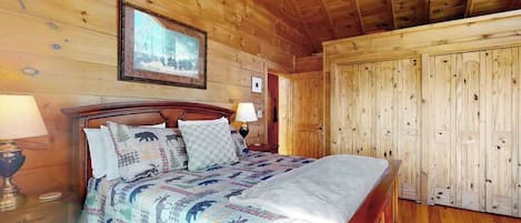 A wooden-paneled room with a bed, a framed picture on the wall, and a wardrobe.