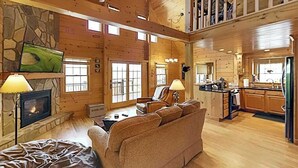A spacious log cabin interior with a fireplace, a television mounted on the wall, a sofa, and a kitchen area. - Luxurious log cabin w/stunning views, WiFi, hot tub + 15 mins to Black Mountain (Old Fort)