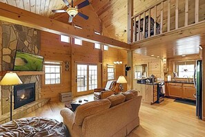 Ein großzügiges Blockhaus-Interieur mit Kamin, Wand-Fernseher, einer Couch und einer Küchenzeile.