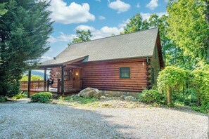 Eine Blockhütte mit Veranda, umgeben von Bäumen und einer Schotterauffahrt.