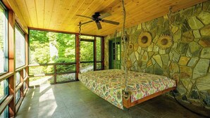 A bedroom with a bed, a ceiling fan, stone walls, and large windows. - Luxurious log cabin w/stunning views, WiFi, hot tub + 15 mins to Black Mountain (Old Fort)