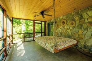 Ein Schlafzimmer mit Bett, Deckenventilator, Steinwänden und großen Fenstern.