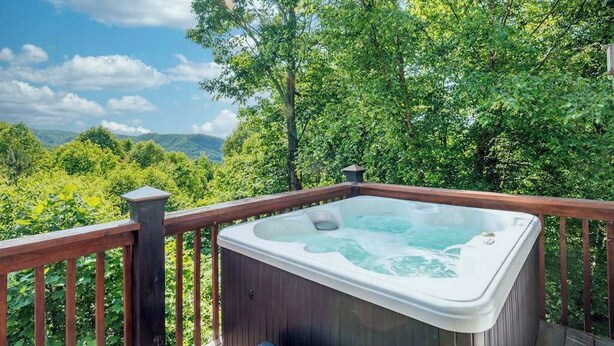 A hot tub on a wooden deck with a forest view. - Luxurious log cabin w/stunning views, WiFi, hot tub + 15 mins to Black Mountain (Old Fort)