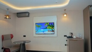 A modern room with a flat-screen TV mounted on the wall, a round table with a chair, a cabinet with a tray of items, and a ceiling light fixture.