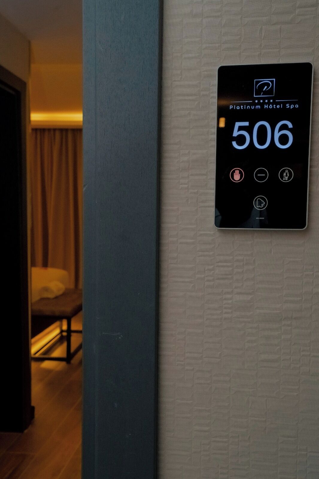 Une chambre d’hôtel équipée d’un écran numérique affichant le numéro de chambre 506, d’un lit, d’une chaise et d’un rideau.
