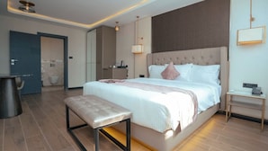 A hotel room with a bed, bedside table, bench, and a bathroom visible in the background.