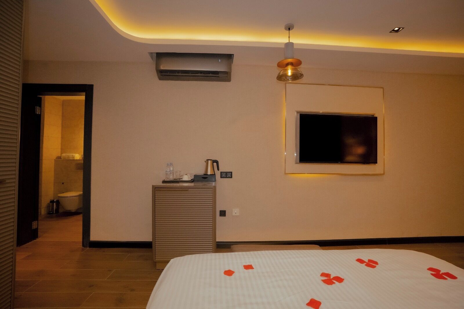 Ein Hotelzimmer mit einem Bett, einem an der Wand befestigten Fernseher, einer kleinen Kommode und einer Klimaanlage.