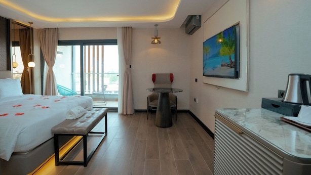 A hotel room with a bed, a desk, a chair, a painting, and a window with curtains.