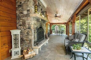 A covered porch with stone walls, a fireplace, wicker furniture, and a view of the outdoors. - Riverside opulence with game room, private heated pool, hot tub & firepit (Rutherfordton)
