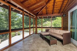 A covered patio with a wooden ceiling, large windows, a beige sofa, and a small table. - Riverside opulence with game room, private heated pool, hot tub & firepit (Rutherfordton)